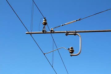Metal pole construction for holding electrical wires at local train station connected through ceramic insulators on clear blue sky background