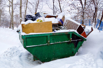 The metal container is filled with garbage, in winter in the snow.