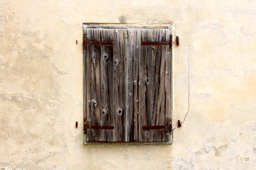 Old wooden window blinds held together with rusted metal hinges mounted on cracked dilapidated house wall on warm sunny day