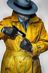 Anonymous  man in a grey fedora pulling out a gun from his trench coat.