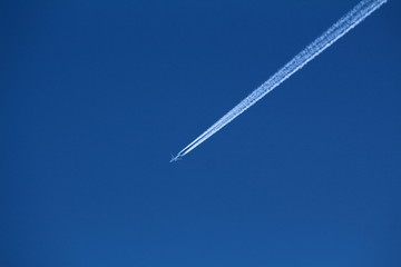 Passenger plane flying at high altitude through clear blue sky leaving two dense white trails on warm sunny day