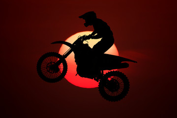 Naklejka na ściany i meble Silhouette of motocross jump in the air with big sun background.