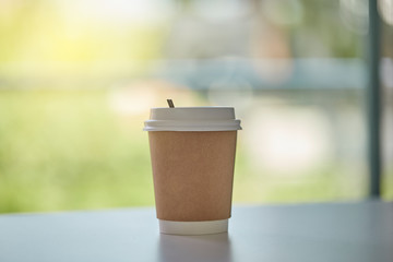 PAPER COFFEE CUP on white counter table see through blur green outdoor background. Close up and selective focus.