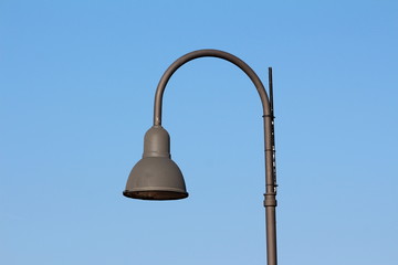 Tall dark grey modern public street lamp with LED light on clear blue sky background