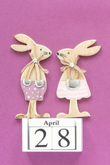 Wooden cubes calendar April 28 and pair of wooden easter bunnies on purple paper background. Concept Christian Easter Template for lettering, text or your design Creative Top View