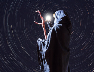 a witch is standing in front of the nocturnal starry sky and looks to Polaris