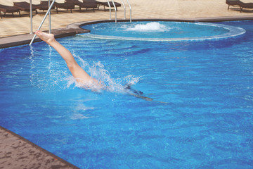 Young cute woman in a black swimsuit and long hair jumps into a pool with blue water.
