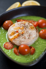 Closeup of baked fish medallions with cherry tomatoes on a bedding of green peas puree, vertical shot