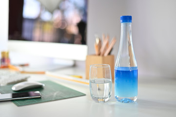 Water bottle and glass of water on office desk.