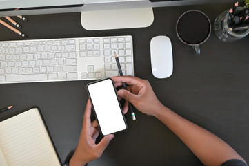 Top view Creative stylish hands holding blank screen mobile phone while working  desktop computer.