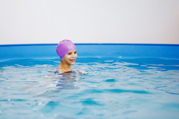 Girl in the lilac hat is having fun, swimming in the pool.