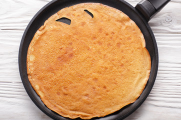Stack of French crepes in frying pan on wooden kitchen table