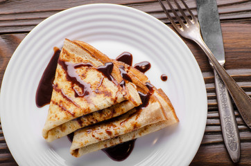 Flat lay French crepes with chocolate sauce in ceramic dish on wooden kitchen table