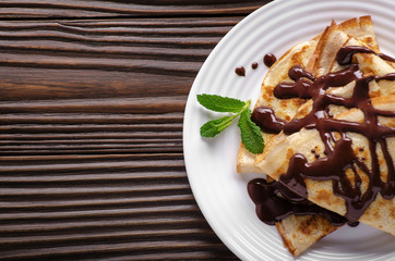 Flat lay French crepes with chocolate sauce in ceramic dish on wooden kitchen table