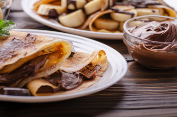 French crepes with chocolate sauce and banana in ceramic dish on wooden kitchen table