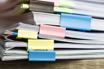 Close up pile of unfinished paperwork on office desk waiting to be managed and inspected. Stack of homework assignment with colorful paper clips. Report papers stacks. Business and education concept.