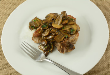 Pork chop with mushroom sauce on white plate with fork