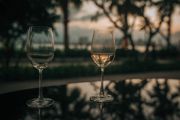  two glasses of wine, in backlight at sunset against a background of palm trees and the sea