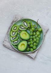 grapes, avocado and kiwi fruit in green rustic plate on marble texture background with copy space