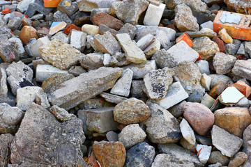 Pile of construction waste grey concrete pieces and old broken bricks lying on construction site as textured industrial background.
