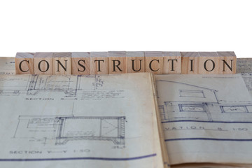 Construction written on wooden blocks on house extension building plans blueprints with a white background