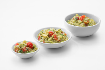 close up view of three plates with guacamole on white back
