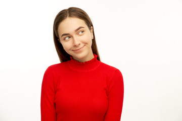 Obraz premium Intriguing young woman, looks mysteriously aside, has brilliant idea in mind. Fomale poses against white studio background with free space for your advertising content