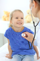 Doctor examining a little girl by stethoscope. Happy smiling child patient at usual medical inspection. Medicine and healthcare concepts