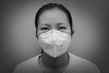 Portrait of Asian woman using N95 respirator mask for protecting air pollution. Black & white tone