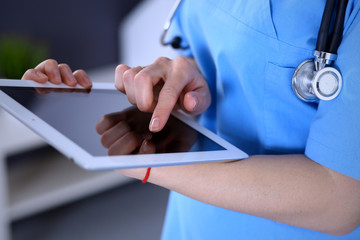 Woman doctor using tablet computer while standing straight in hospital office, closeup. Healthcare,...