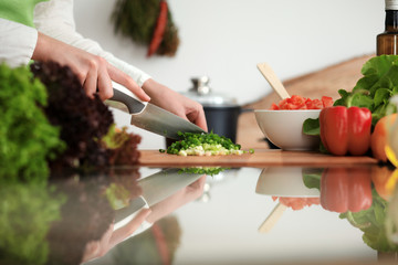 Unknown human hands cooking in kitchen. Woman slicing green onion. Healthy meal, and vegetarian food concept