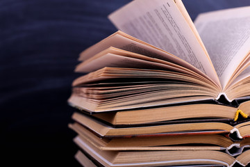 Open books are a stack on the desk, against the background of a chalk board. Difficult homework at school, a mountain of knowledge.