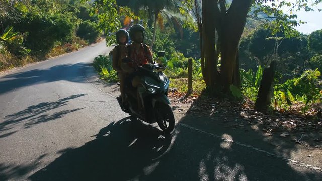 Young beautiful tourist couple rides the jungle on a scooter wearing helmets. Travel, freedom, happiness, vacation, honeymoon concept.