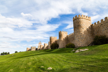 Fototapeta na wymiar View of the medieval city walls surrounding the city of Avila, Spain, and the green lawn in front of Puerta del Carmen. Called the Town of Stones and Saints, Avila is a UNESCO World Heritage Site