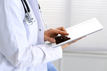 Woman doctor using white tablet computer while sitting at chair in hospital, close-up