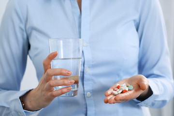 Young unknown woman holding pills and glass of water, closeup of hands.  Medicine and healthcare concept