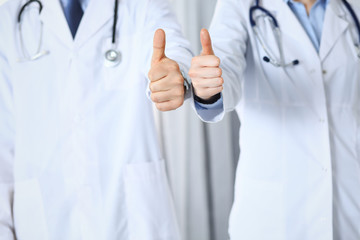 Team of unknown medicine doctors showing OK sign with thumb up close up. Success and high level service in health care, best treatment and customer loyalty and physical concept