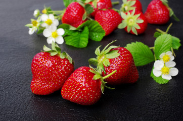 Ripe strawberries with flowers and leaves on a dark background