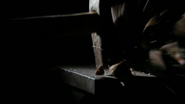 man smashes nuts with a hammer on the anvil in slow motion on black bg