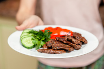 Close-up serving homemade grilled beef medallions with grilled pepper, fresh cucumber and parsley on a round white plate. Concept dinner at home with family