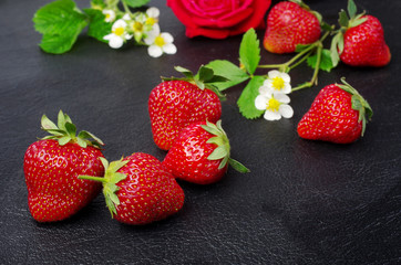 Ripe strawberries with flowers and leaves in a wooden bowl on a dark background