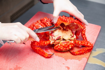 Cook in uniform is carving fresh red big boiled prepared blue kamchatka crab with scissors. Concept useful seafood in menu, chef of restaurant preparing crab for serving for guests, clients