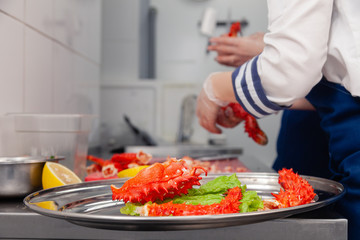 Cook in uniform is carving fresh red big boiled prepared blue kamchatka crab with scissors. Concept useful seafood in menu, chef premium restaurant preparing crab for serving for guests, clients