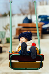 happy boy riding on a swing in a jacket hat and scarf