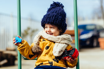 happy boy riding on a swing in a jacket hat and scarf
