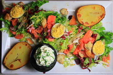 plate of lettuce salad with salmon, mimosa eggs, potatoes and sauce, diet dish