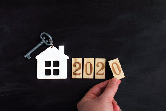 model of a house with a key next to the number 2020 and a hand. build individual housing in the new year