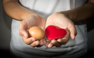 Red heart and egg in woman hand.
