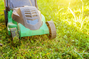 Lawn mower cutting green grass in backyard in sunny day. Gardening country lifestyle background. Beautiful view on fresh green grass lawn in sunlight, garden landscape in spring or summer season