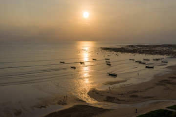 Aerial drone view of sunset over a shallow, tropical ocean with traditional wooden longtail boats at anchor